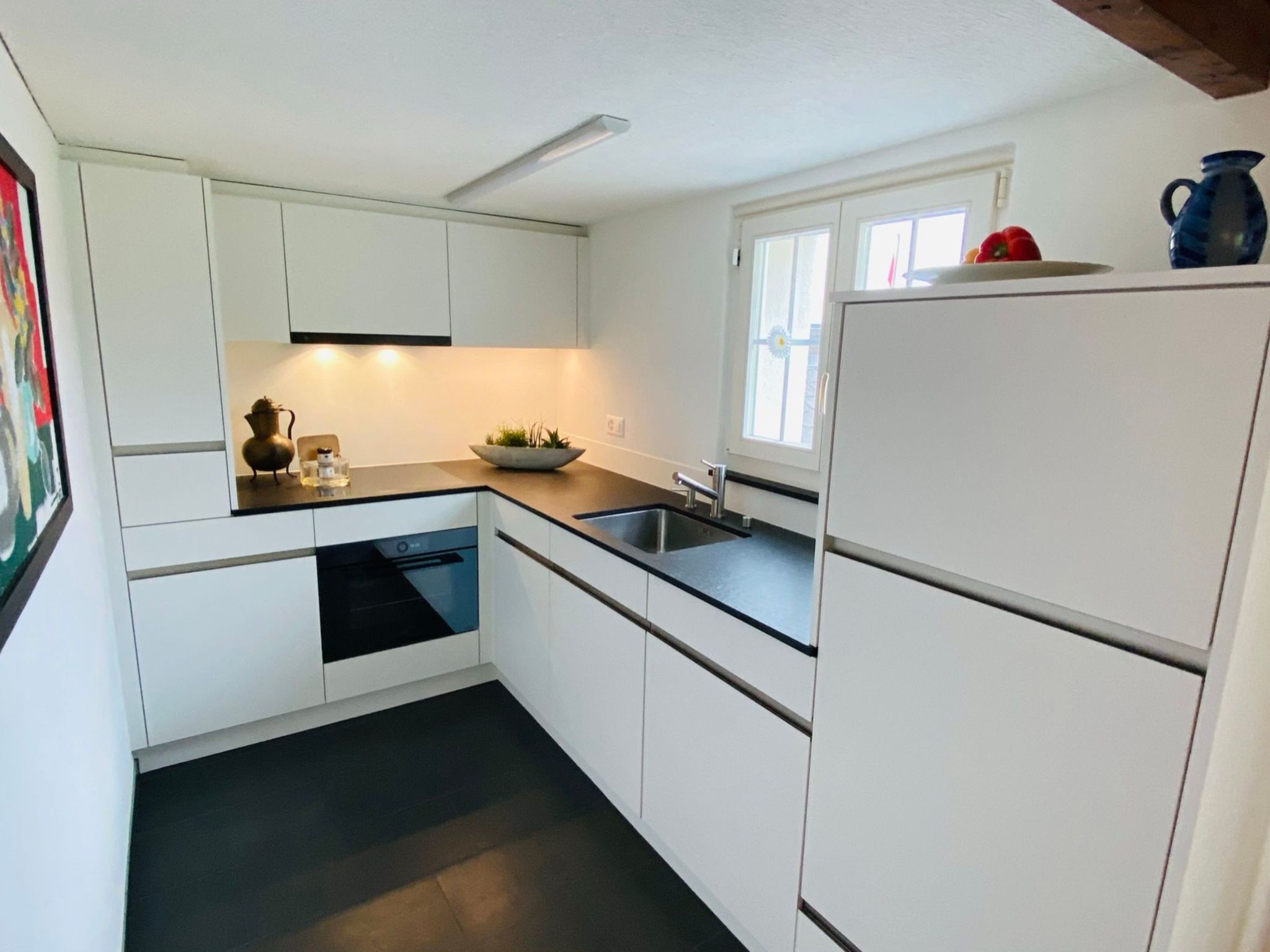 A compact kitchen with white cabinetry, a built-in dishwasher, a sink, and a window with a view.