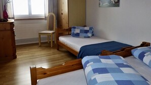 Een kamer met twee houten bedden, een stoel, een houten dressoir en een raam met gordijnen.