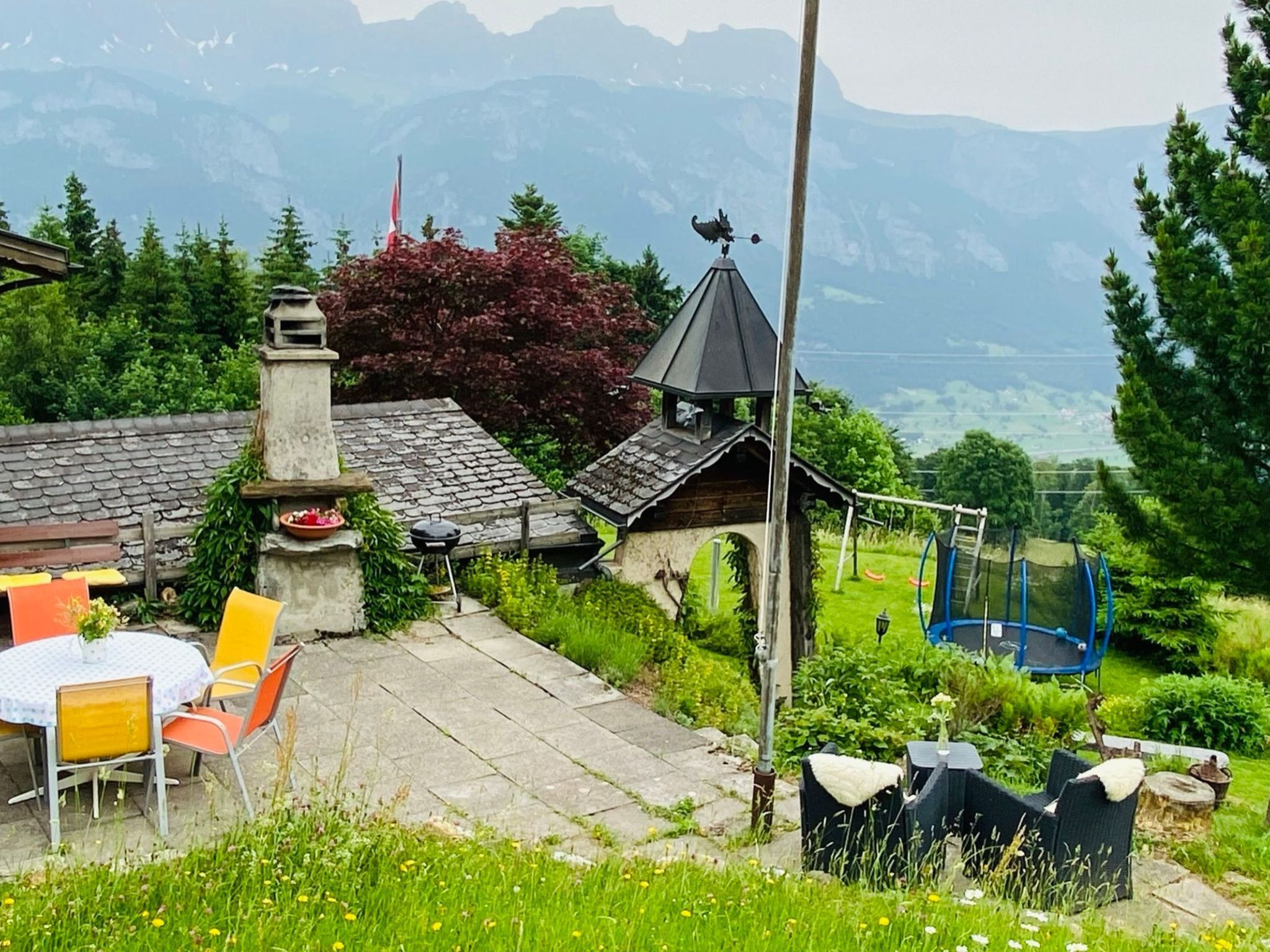 A rustic chalet with a stone chimney, a wooden porch, and a view of mountains in the background.