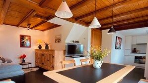 Een ruime eetruimte met een grote houten tafel, twee hanglampen en een keuken op de achtergrond.