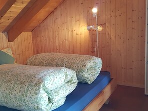 A room with wooden walls and a sloped ceiling, featuring two beds with floral bedding and a blue mattress.