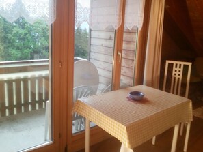 A small room with a table and chairs, a window with a view of trees, and a balcony with a railing. - Schwendihof, (Flumserberg Tannenheim), by Interhome (Flumserberg Tannenheim)