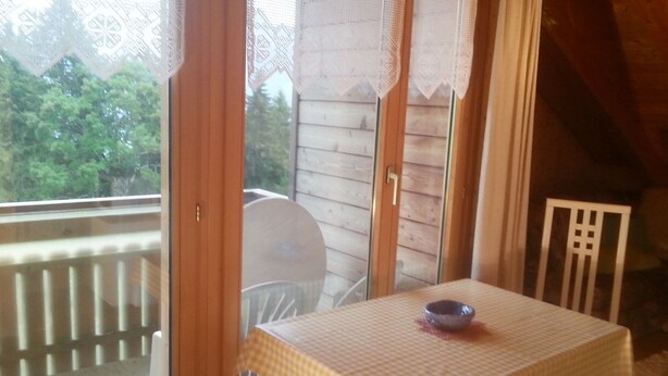 Ein Zimmer mit kariertem Tisch, einem Stuhl, einem Fenster mit Blick ins Grüne und einer Holzbalkendecke.