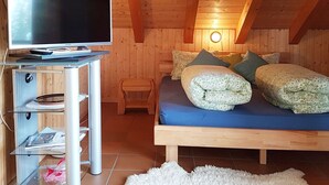 Ein gemütliches Schlafzimmer im Dachgeschoss mit einem Bett, einem Fernseher auf einem Standfuß und einem kleinen Holzstuhl.