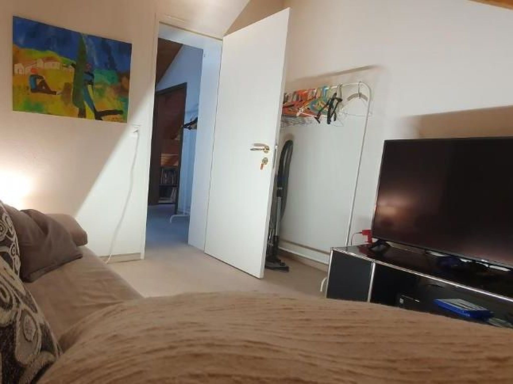 Une chambre à coucher avec un lit, une télévision, une armoire et un tableau au mur.