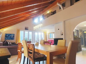 Un comedor con mesa y sillas de madera, una araña y vistas al exterior a través de amplios ventanales.