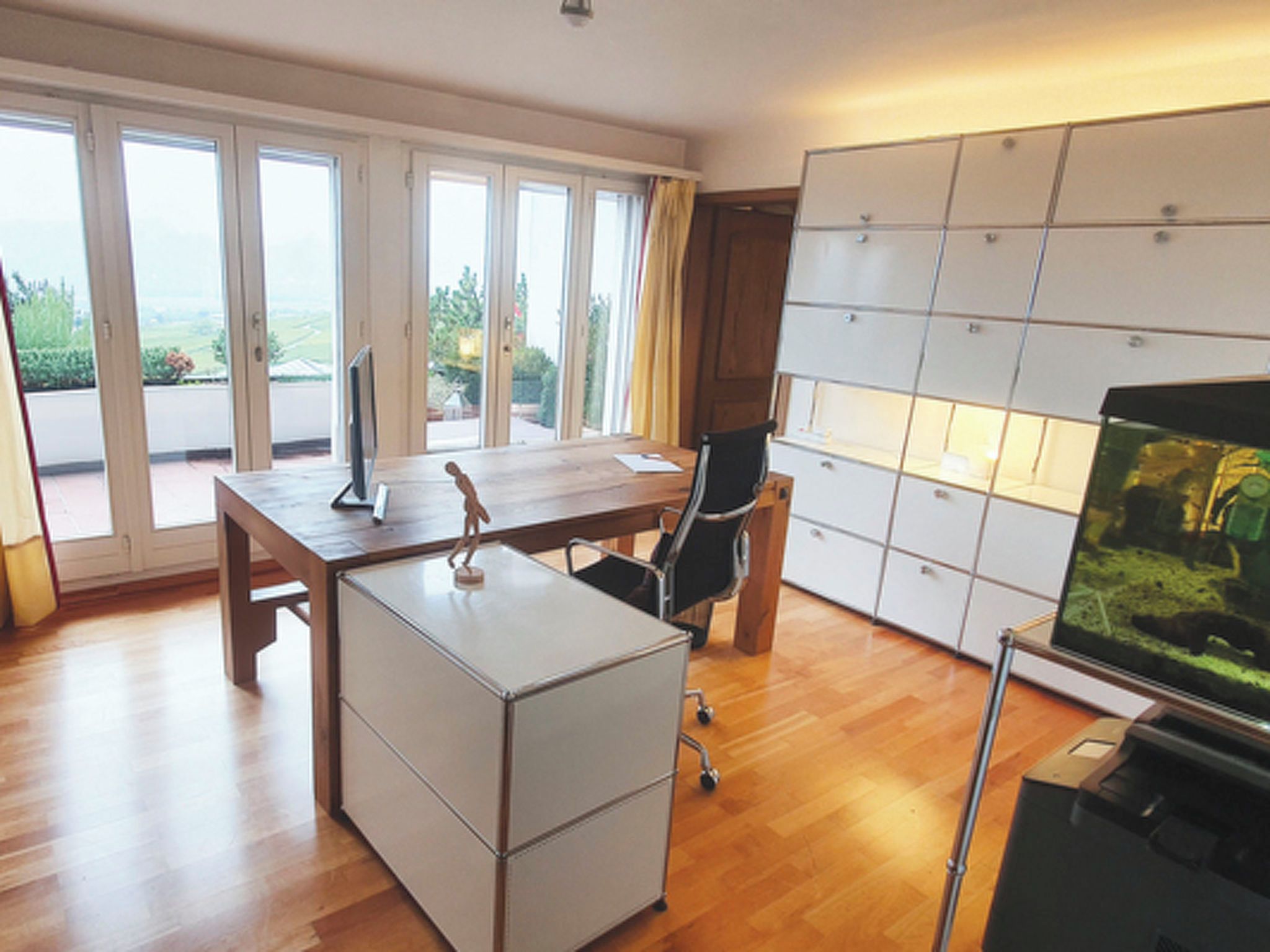 Ein moderner Arbeitsraum mit Schreibtisch aus Holz, Bürostuhl und einem großen Aquarium.