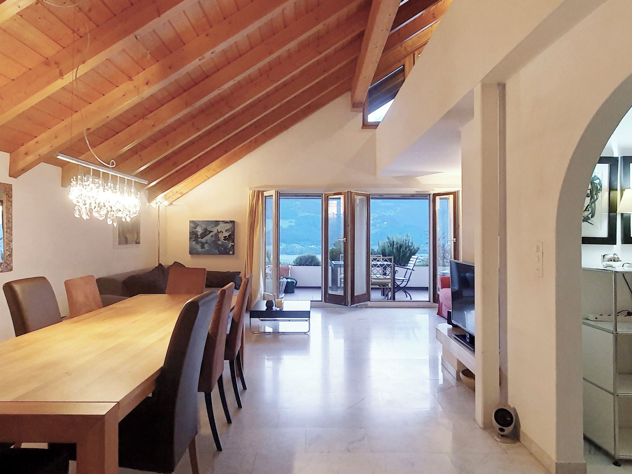 Un comedor espacioso con una mesa y sillas de madera, una lámpara de araña y vistas al exterior a través de grandes puertas correderas.