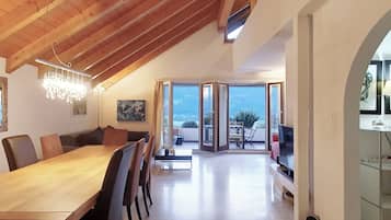Uma ampla área de refeições com mesa e cadeiras de madeira, um lustre e vista para o exterior através de grandes portas deslizantes.