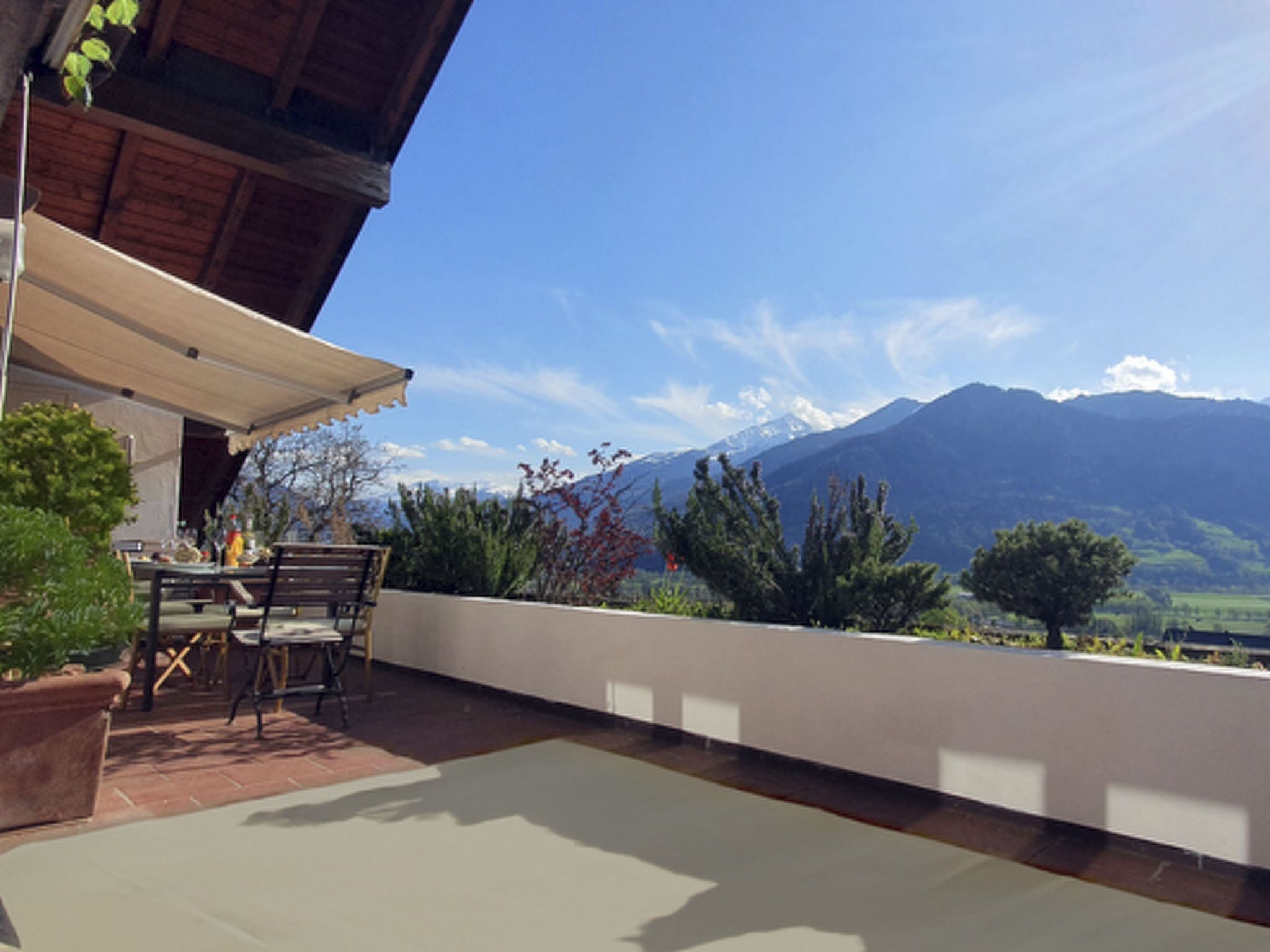 Eine Terrasse im Freien mit Tisch und Stühlen, einer hölzernen Pergola und Blick auf die Berge.