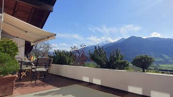 Eine Terrasse im Freien mit Tisch und Stühlen, einer hölzernen Pergola und Blick auf die Berge.
