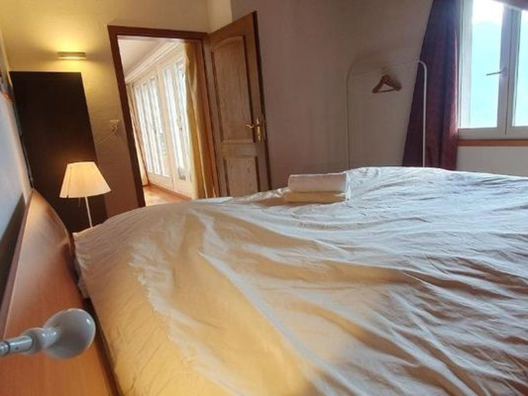 Une chambre d’hôtel avec un lit, une table de chevet, une lampe, une fenêtre et une porte.