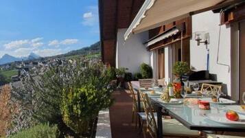 Un espace de restauration en plein air avec une table dressée pour deux personnes, offrant une vue sur un paysage montagneux.