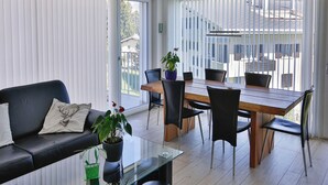 Ett modernt vardagsrum med ett soffbord i glas, en svart soffa och en matplats med ett bord och stolar i trä.