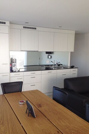 A modern kitchen with white cabinets, a black countertop, and a wooden dining table with two chairs.