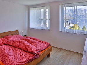 Una camera da letto con un letto, due finestre con tende e vista sulle montagne.