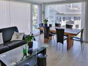 A modern living room with a glass coffee table, black leather sofa, and a dining area with a wooden table and chairs.