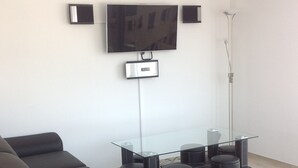Ett modernt vardagsrum med en platt-TV som är monterad på väggen, ett soffbord med glasskiva, svarta soffor och en golvlampa.