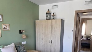 Et soveværelse med seng, skab, natbord, lampe og spejl.
