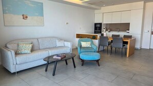 Un salon avec un canapé, une table basse et un fauteuil bleu. Il y a également un coin cuisine avec une table à manger et des chaises.