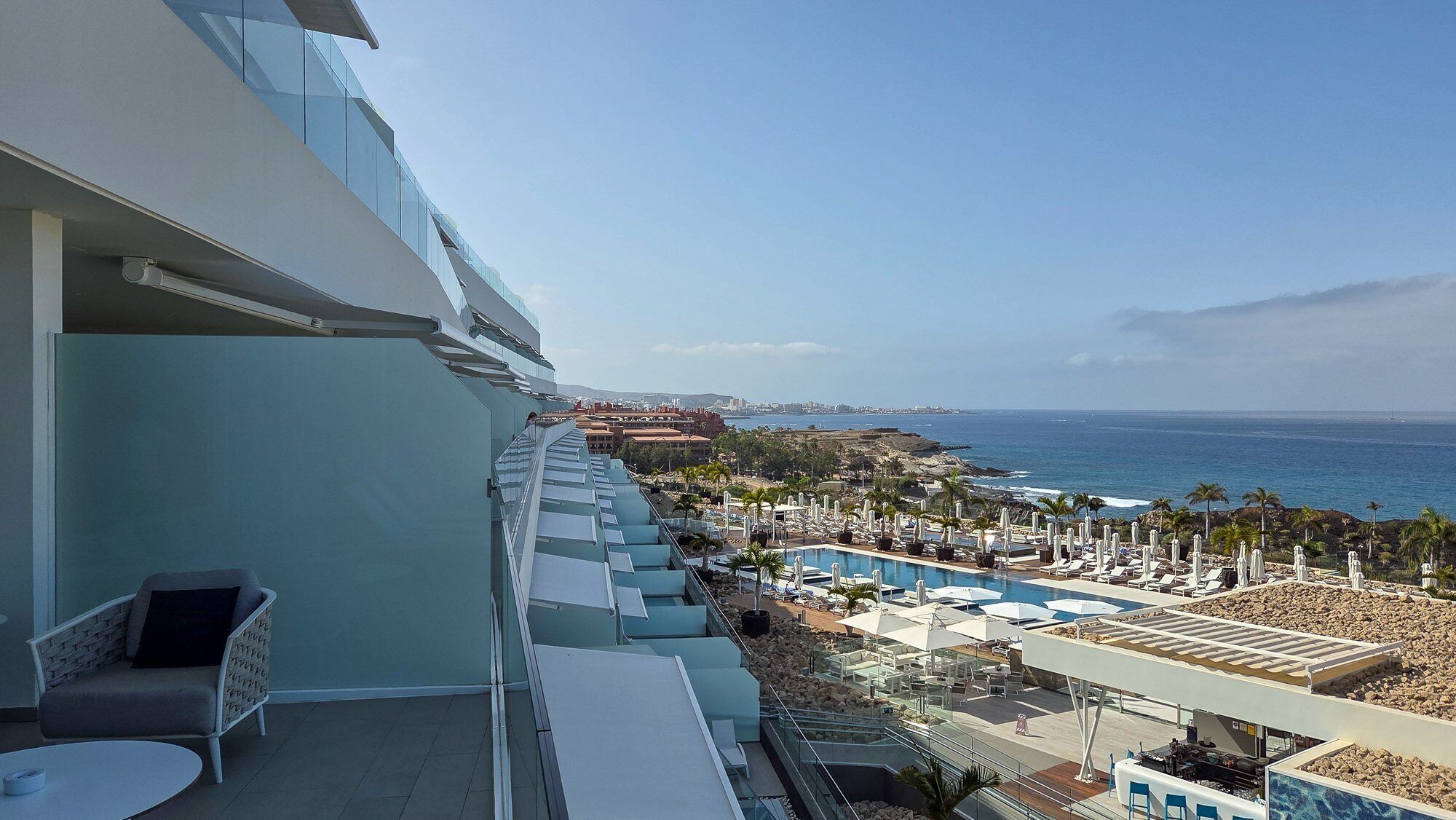 Un balcon avec une piscine, des chaises longues et une vue sur l’océan et le paysage urbain.