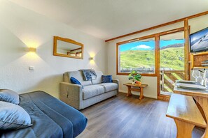 A cozy room with a sofa, a small table with a plant, and a TV on a wooden stand. - Residence Cuzco (Les Belleville)