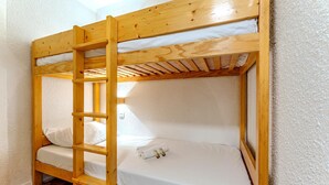 Een stapelbed met een houten ladder, wit beddengoed en een zichtbare elektriciteitsaansluiting op het onderste bed.