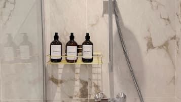 A bathroom with a shower, a glass door, and a shelf with three bottles of toiletries.