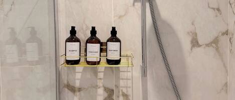 Un baño con ducha, puerta de cristal y estante con tres artículos de tocador.