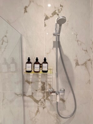 A bathroom with a shower, a glass door, and a shelf with three bottles of toiletries. - Island Club Guest House (Sliema)