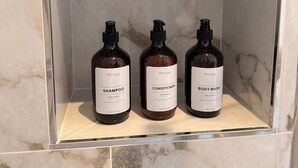 A bathroom shelf with three bottles of personal care products: shampoo, conditioner, and body wash. - Island Club Guest House (Sliema)