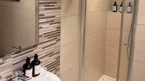 A modern bathroom with a glass shower enclosure, a sink with toiletries, and a mirror. - Island Club Guest House (Sliema)