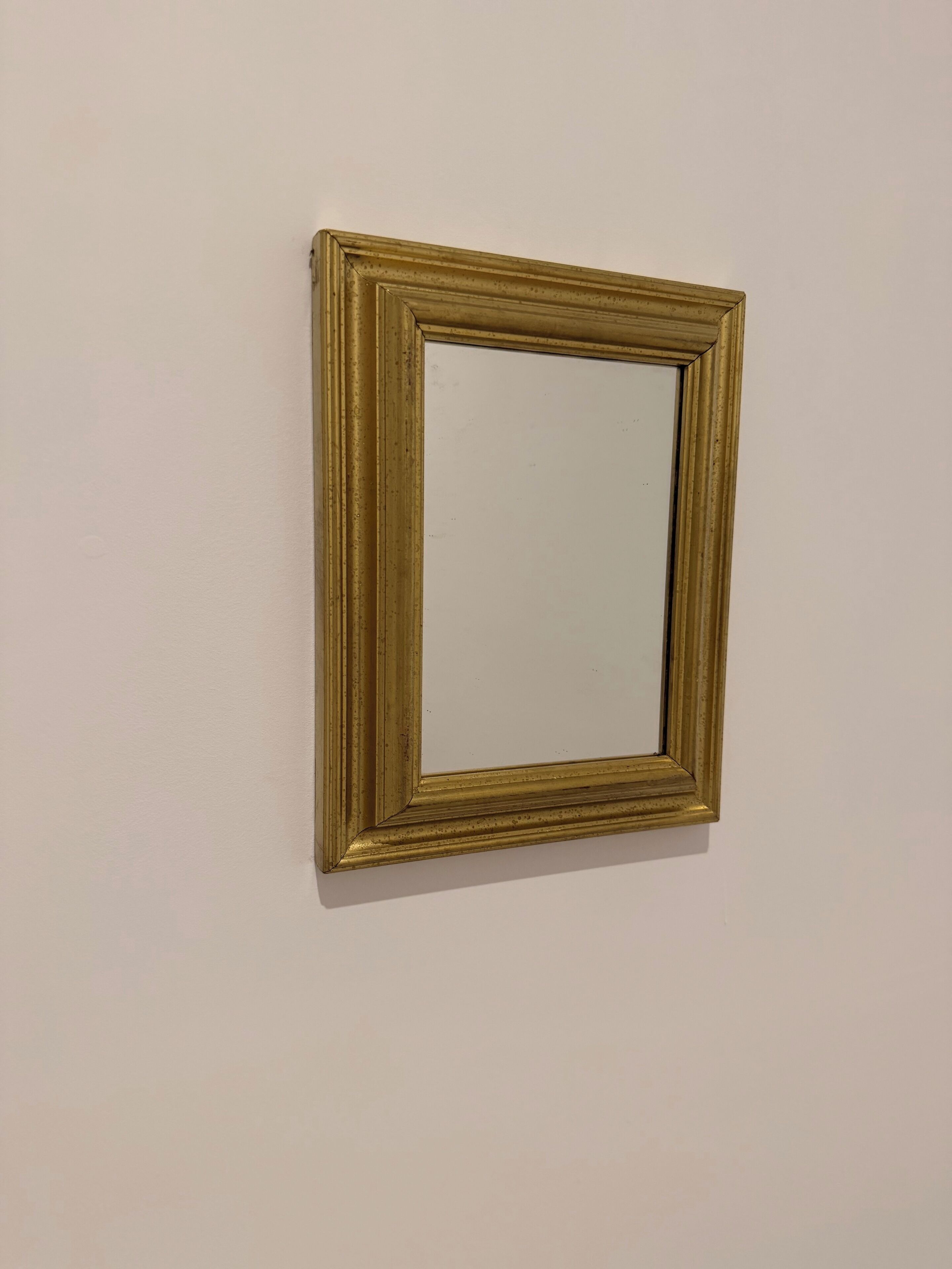 Ein gerahmter Spiegel mit goldener Rahmung an einer schlichten Wand.