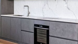 Een moderne keuken met grijze kastjes, een witte marmeren spatwand en een ingebouwde vaatwasser.