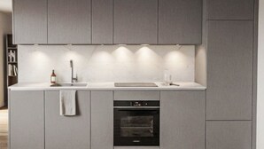 Et moderne køkken med lysegrå skabe, en indbygget ovn og en bordplade med vask og en flaske.