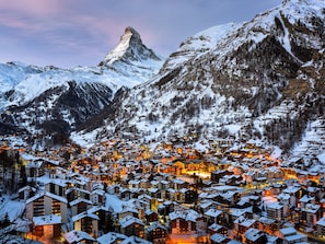 Eine verschneite Bergstadt mit Gebäuden und einem markanten Gipfel im Hintergrund.