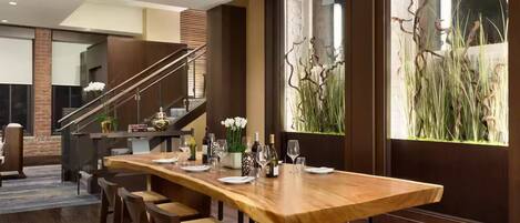 A modern dining area with a long wooden table, multiple chairs, and a staircase in the background.