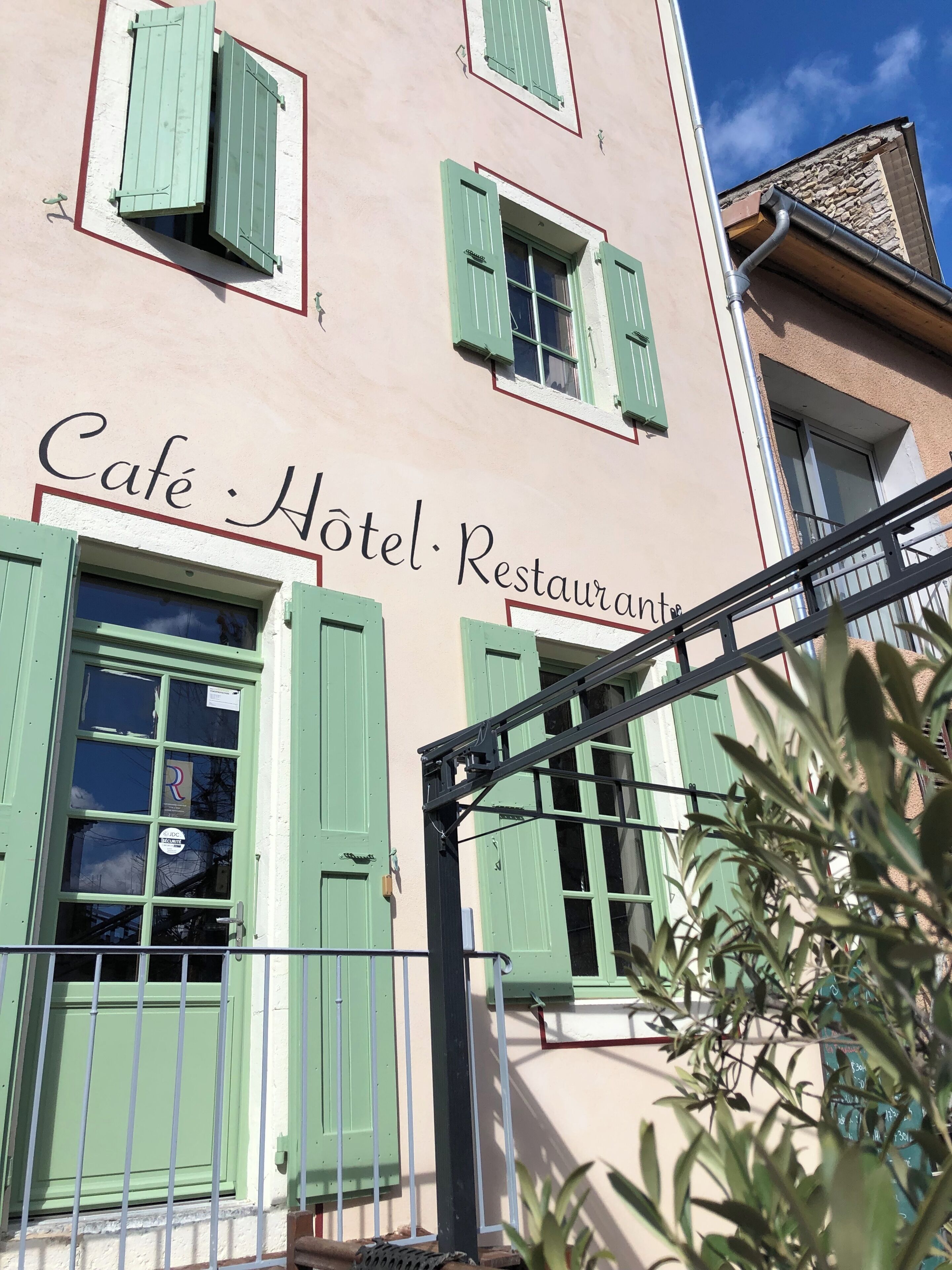 A building with green shutters and a sign reading 'Cafe Hotel Restaurant.'