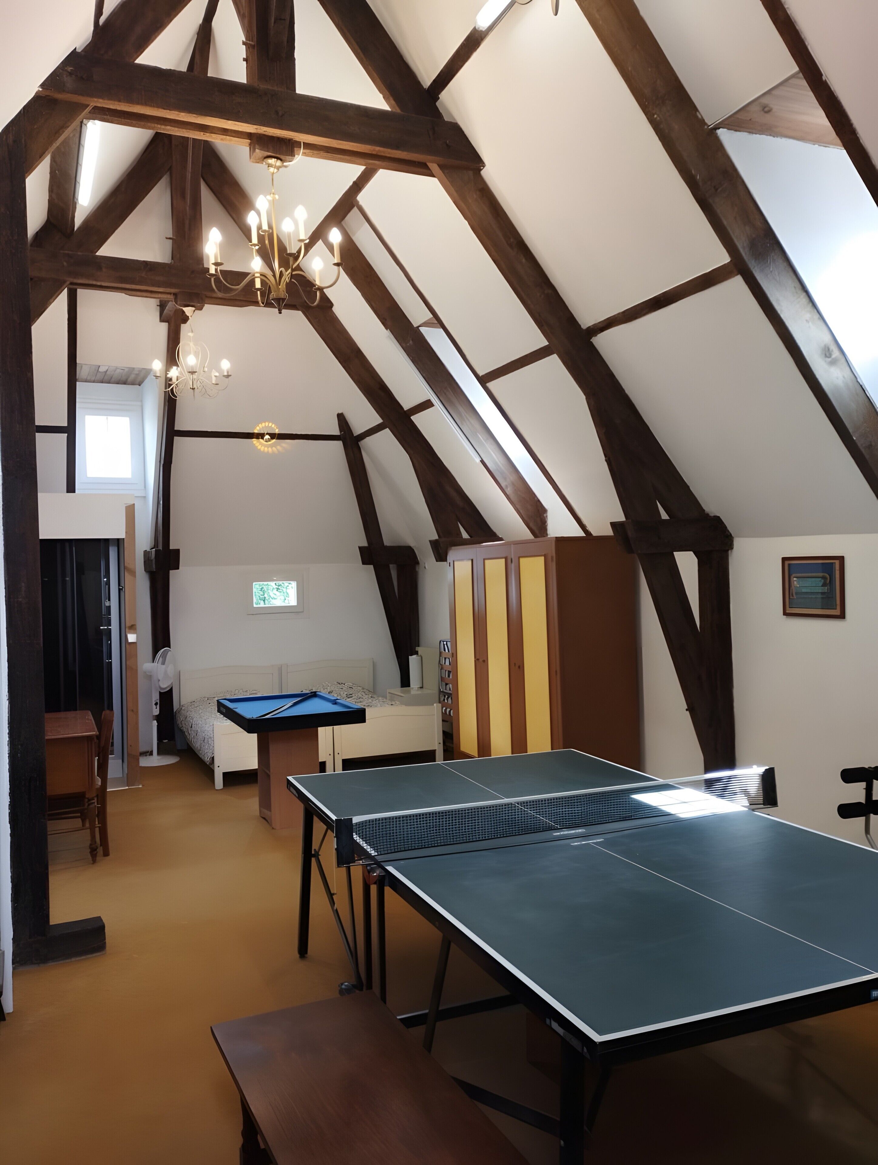 Habitación en el ático con mesa de ping pong, cama, ventilador y candelabro.
