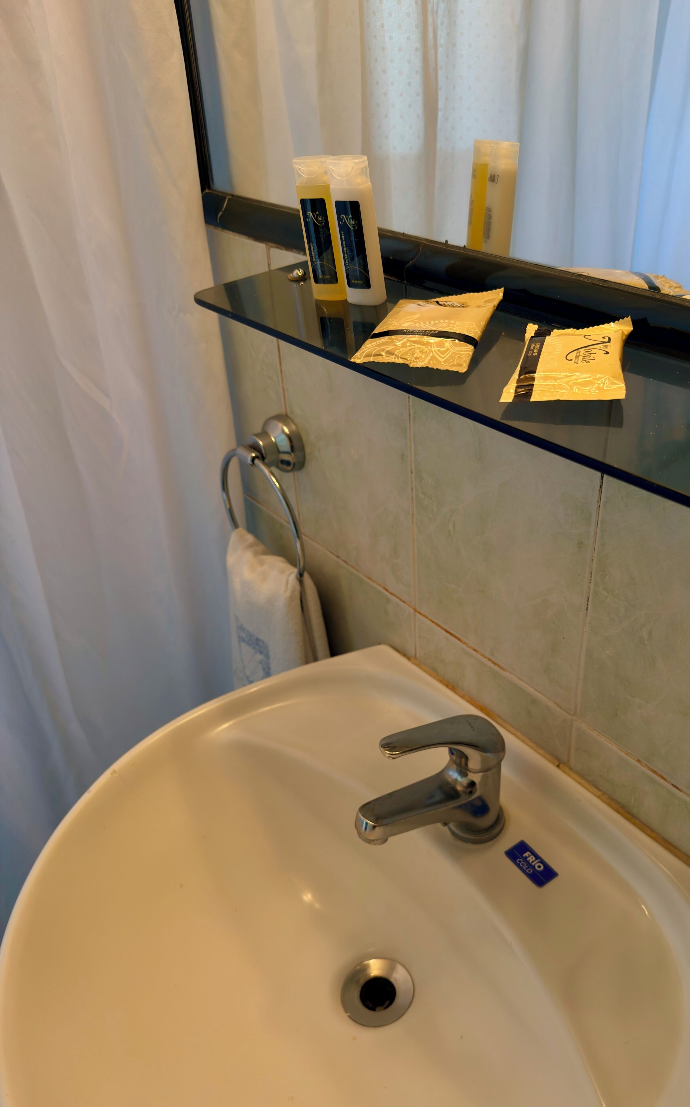 A bathroom with a glass shelf holding toiletries, a sink with a faucet, and a towel rack.