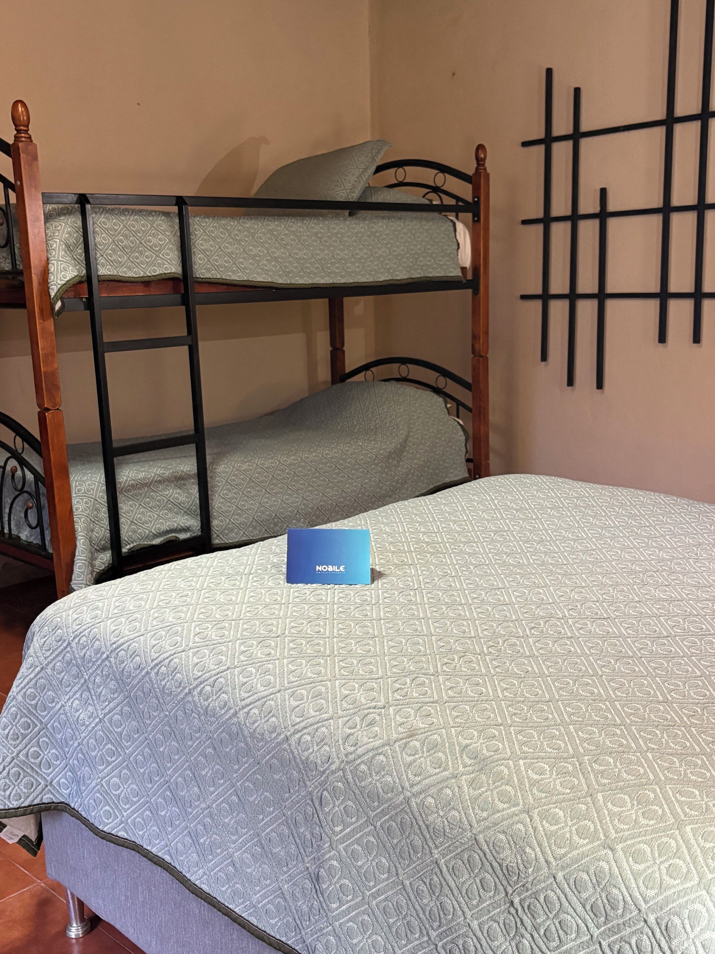 Una litera con una etiqueta azul en la cama inferior, una colcha estampada y una pared decorada con un diseño geométrico.