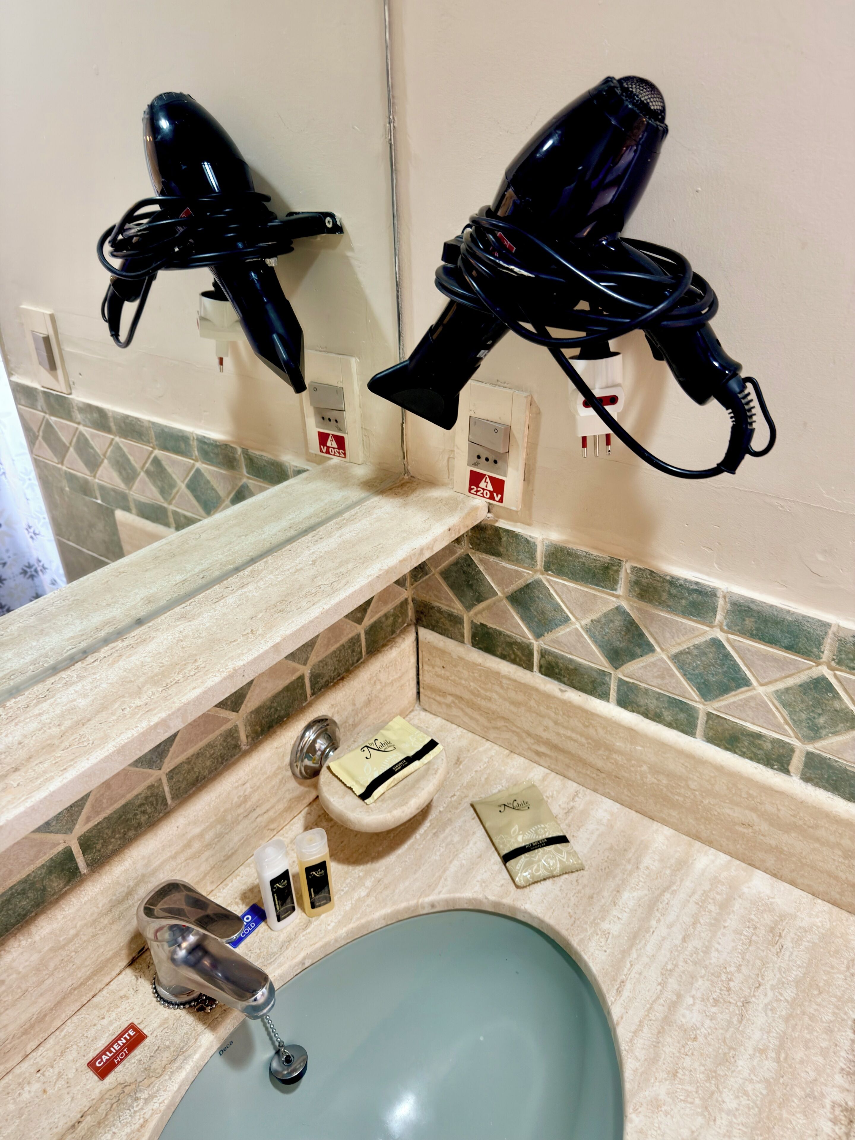 Un bany amb un lavabo, dos assecadors de cabell penjats a la paret i un dispensador de tovalloles.