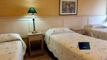 Una camera d'albergo con due letti singoli, un comodino con una lampada, un quadro appeso al muro e un libretto blu su uno dei letti.