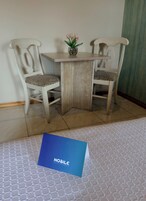 Una habitación pequeña con una mesa de madera y dos sillas, un florero con flores y una tarjeta azul en el suelo.