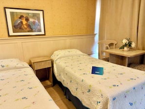 Habitación de hotel con dos camas, una mesita con un jarrón de flores, un cuadro en la pared y una silla.