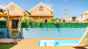 Una piscina con tobogán, rodeada por una terraza de madera y una valla verde.