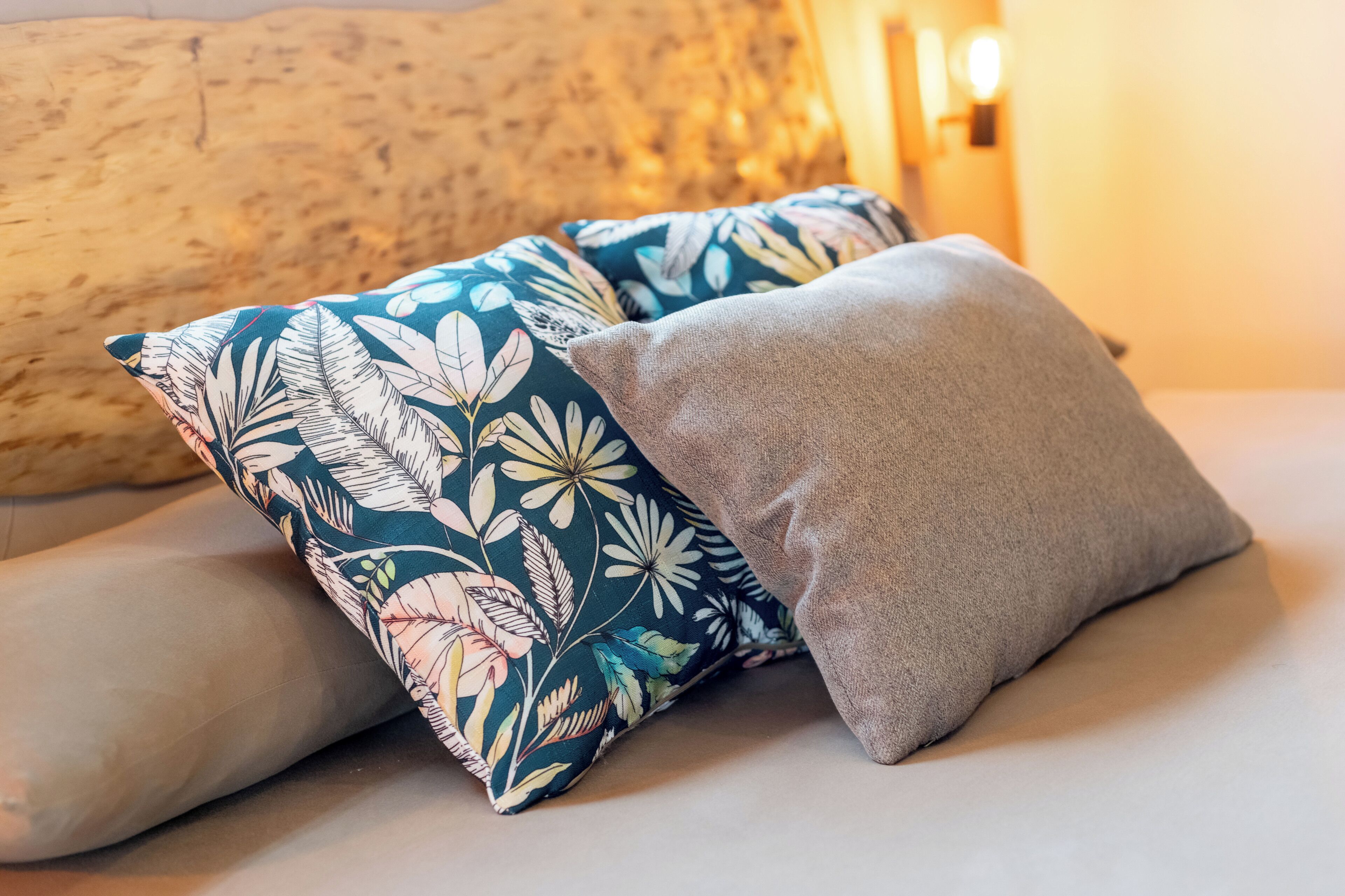 Una cama con dos almohadas, una con estampado floral y otra lisa.