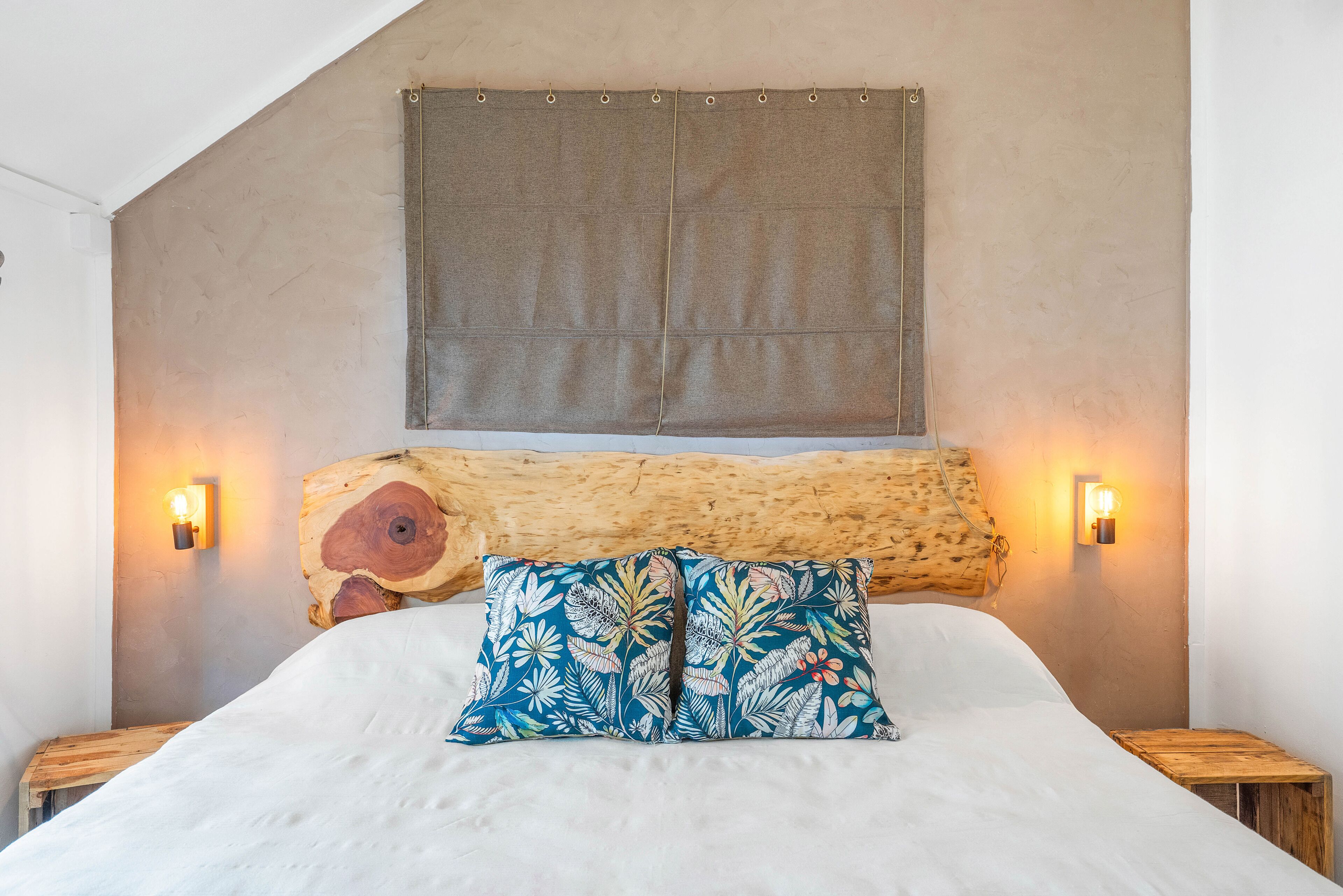 Un dormitorio con cama, almohadas, cabecero e iluminación en la pared.
