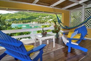 A balcony with blue chairs, a white table, and a view of a coastal area with buildings and greenery. - Beachfront Living & Local Island Life (Laborie)
