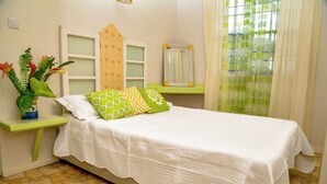 Ein Schlafzimmer mit Bett, Nachttisch, Spiegel, Fenster mit Vorhängen und einer Pflanze.